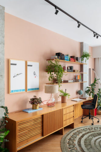 Décor colorido, sala com home office e cozinha integrados em apartamento com 121m2 em Copacabana. A parede da estante e prateleira do home office é pintada de rosa.