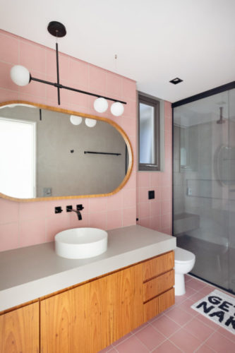 Banheiro com azulejos na cor rosa, espelho oval com borda em madeira.