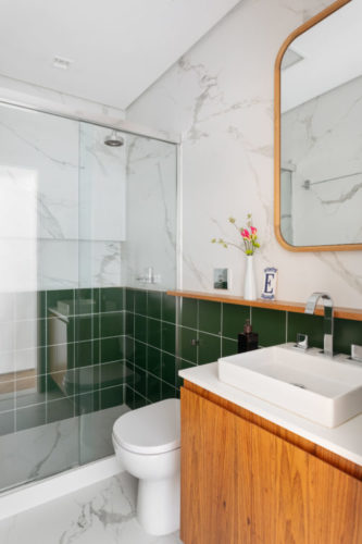 Banheiro revestido em meia parede com azulejos verdes, e na parte de cima, porcelanato com estampa de mármore.
