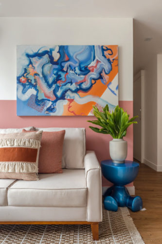 Sofá bege, na parede atrás, duas faixas na horizontal, uma pintada de branco e a outra na cor rosa.