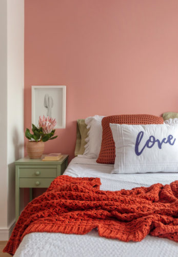 Quarto com a parede atrás da cama pintado de rosa.