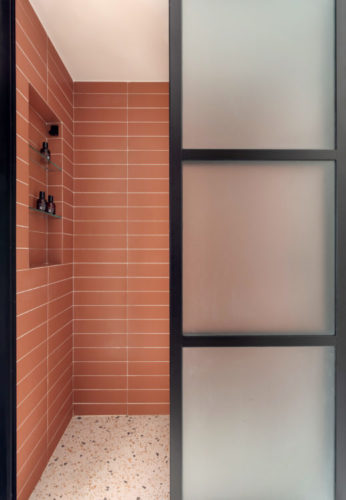 Banheiro com esquadria preta, piso imitando granilite e as paredes revestidas com uma cerâmica retangular na cor goiaba