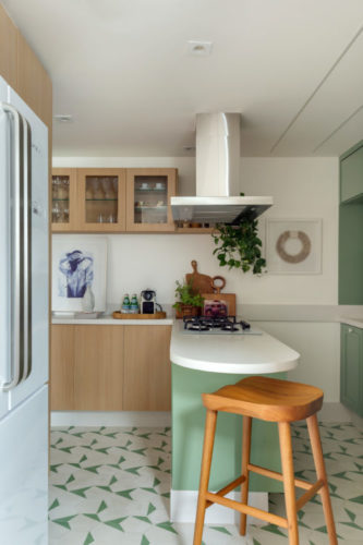 Cozinha com armários na cor verde menta em uma metade do espeço, na outra, os armários em madeira clara. Uma ilha separa os ambientes.