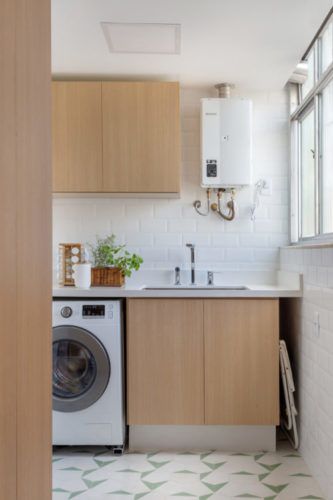 Área de serviço com maquina de lavar embutida e armários em madeira clara 