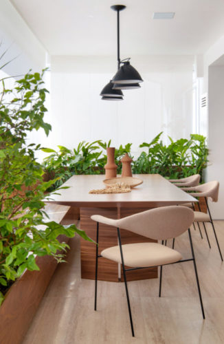 Varanda integrada a sala, que abrigou o espaço para a mesa de jantar. Plantas ao redor de uma banco de madeira em toda a extensão da varanda