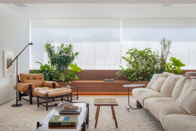Living com a varanda integrada a sala, um banco de madeira em toda a extinção da janela, e móveis de design, como a poltrona Mole de Sérgio Rodrigues por exemplo