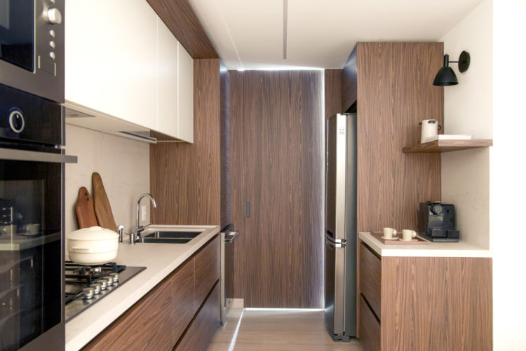 Cozinha longa e estreita, com armários e portas de ligação em madeira. Torre que abriga forno e micro-ondas embutidos.