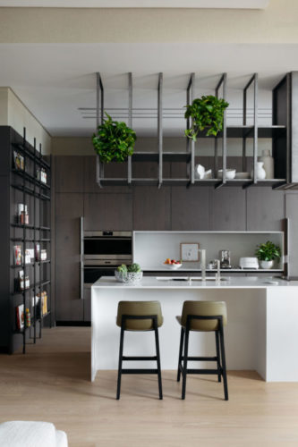 Casa em Miami de 400 m2 foi totalmente reformada. Cozinha integrada a sala de estar. Com os armários em cor escura, bancada branca e estrutura gradeada em aço em cima,