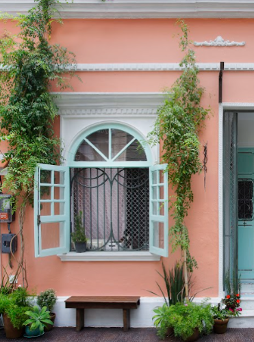 Uma charmosa casa de vila, com a fachada pintada de rosa, porta e janela na cor azul clara.