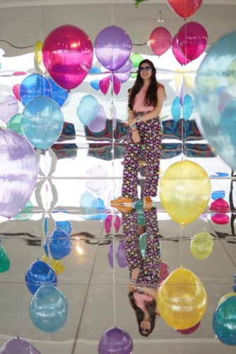 Foto da artista plástica Flavia Junqueira em meio a balões coloridos