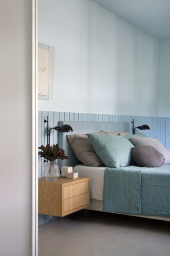 Quarto de casal, com a parede de fundo da cama revestida em meia altura, com ripas de madeira pintadas em azul claro, cabeira da cama em tecido na mesma cor.