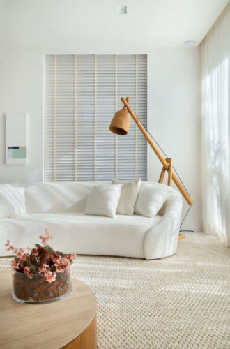 Décor minimalista, sofá curvo branco, luminária de pé em madeira, janelas embutidas na parede, com persianas em lâminas de madeira branca
