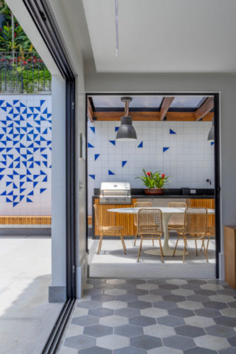 Casa no horto com sala aberta para a área externa, com churrasqueira e ao fundo, painel com azulejos decorados em branco e azul.
