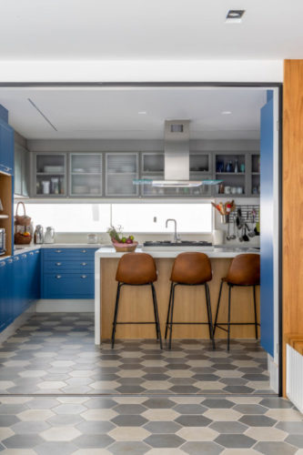 Cozinha aberta para a sala de tv. Com armários azuis e piso cinza com ladrilho hexagonal