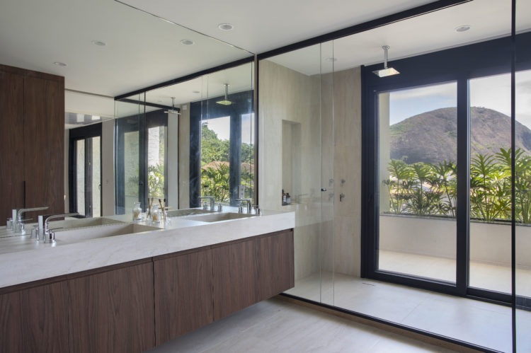 Banheiro grande, com bancada com duas cubas e box bem amplo com chuveiro de teto e esquadrias pretas.