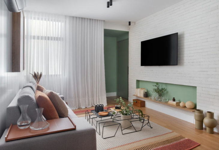 Na sala , o nicho verde na parede sob a tv, que abriga não apenas os equipamentos de áudio, mas também alguns elementos decorativos, sem comprometer a circulação da sala compacta.