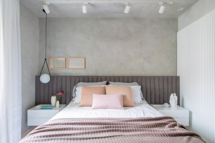 Quarto com meia parede pintada com efeito cimento queimado, cabeceira da cama ao longo de toda a parede, em tecido cinza.