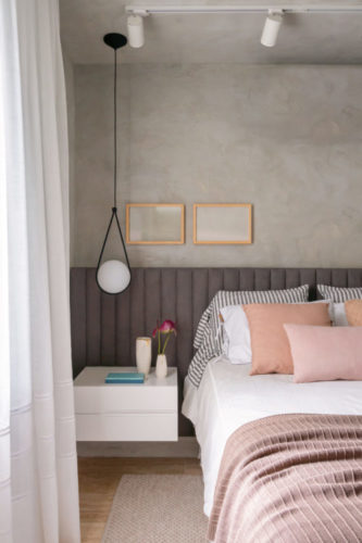 Quarto com meia parede pintada com efeito cimento queimado, cabeceira da cama ao longo de toda a parede, em tecido cinza.