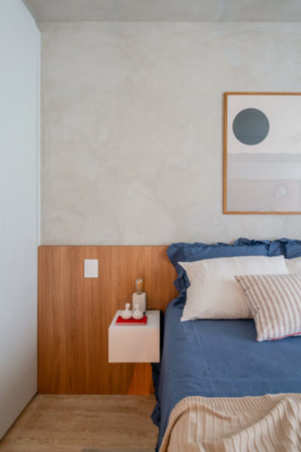 Quarto com meia parede pintada com efeito cimento queimado, cabeceira da cama ao longo de toda a parede, em madeira clara