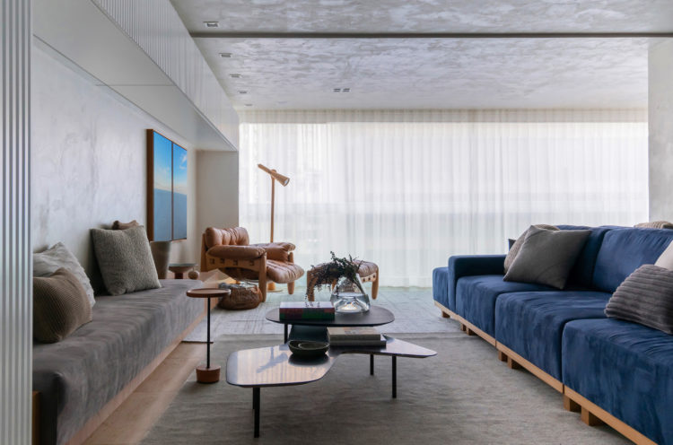 Living decorado com um sofá azul , teto e parede pintados com efeito que imita cimento queimado.