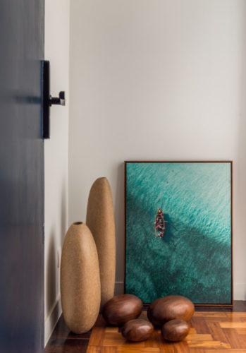 Composição de décor. Um quadro com uma foto de um barquinho no mar, encostada no chão, e na frete, alguns vasos em cerâmica.