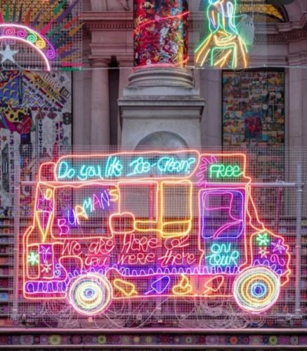 Obra de Chila Kumari, desenho em neon de um tuk tuk. Artista multimídia, nasceu em Liverpool, mas suas memórias estão enraizadas nas tradições de sua família indiana, ela resgata o tuk-tuk onde seus pais vendiam sorvete e cobre a fachada do Tate, em 2020, com imagens vividas, em neon.
