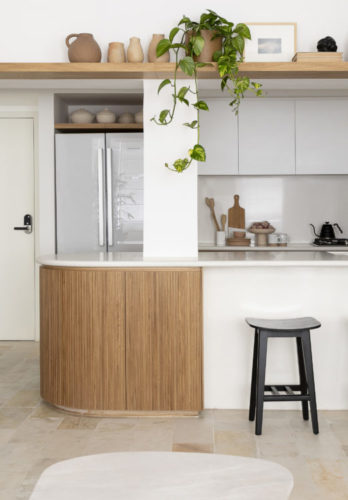 Cozinha aberta para a sala, com balcão branco e a ponta arredondada em madeira