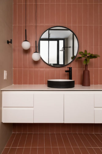 Banheiro com revestimento na cor de tijolo, bancada branca e espelho redondo 