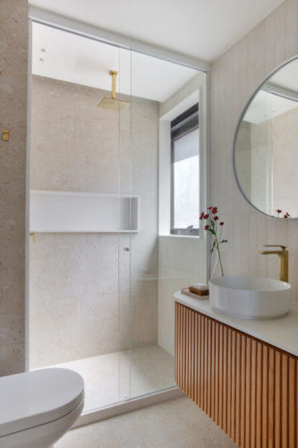 Banheiro revestido em porcelanato claro e armário em ripa de madeira