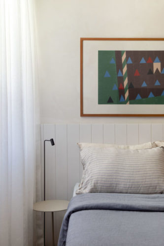 Quarto decorado com tons claros, cabeceira da cama em ripas de madeira branca.