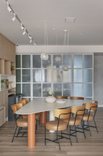 Mesa triangular com lugar para oito cadeiras, ao fundo, porta estilo camarão, com vidro jateado e esquadria branca, separa a sala da cozinha, e quando aberta, permite integração total.