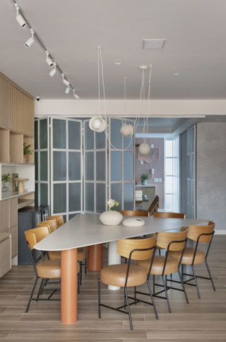 Mesa triangular com lugar para oito cadeiras, ao fundo, porta estilo camarão, com vidro jateado e esquadria branca, separa a sala da cozinha, e quando aberta, permite integração total.