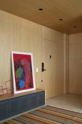Hall de entrada todo revestido em madeira, rack baixo com um quadro apoiado nele e encostado na parede.