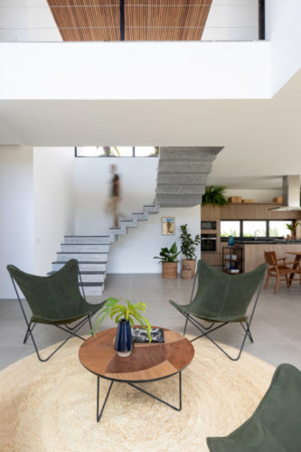 Ambiente da sala em uma casa de praia. Quatro cadeiras "borboletas" em brim verde e uma mesa de centro redonda criam um ambiente.