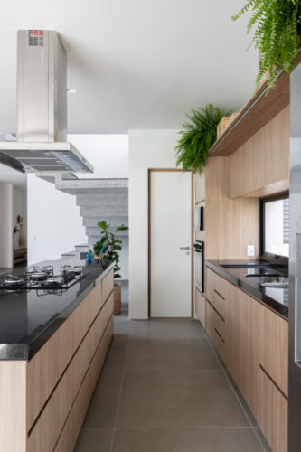 Cozinha com planta "corredor". Bancadas pretas e armários em madeira.