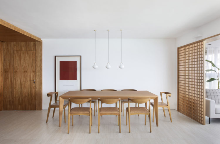Sala de jantar, mesa e cadeiras em madeira, ao fundo, uma grande tela retangular encostada na parede e no piso, colocada fora do eixo 