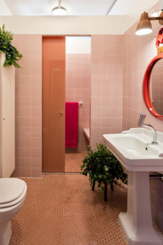 Banheiro revestido com azulejos rosa e piso em pastilha hexagonal