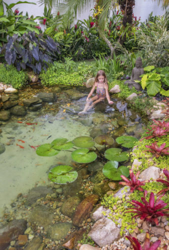 Lago artificial, com carpas e ninfeias, em meio a um jardim de uma casa no Rio de Janeiro. Na foto, uma menina sentada no lago.