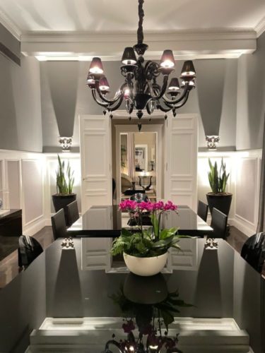 Sala de jantar decorada; paredes cinzas, boiseries brancas em meia parede, mesa de jantar em laca brilhante preta e lustre preto