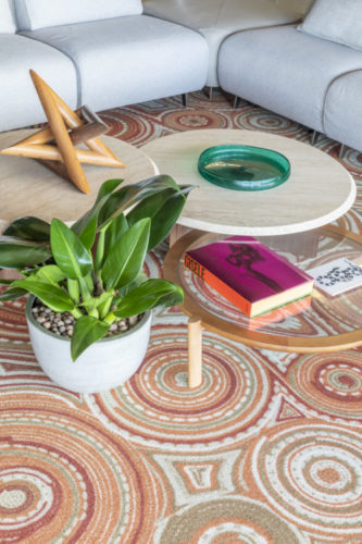 Mesas de centro redondas com alturas diferentes, compondo uma produção de decoração. Um vaso de planta ao lado..embaixo das mesas, um tapete colorido