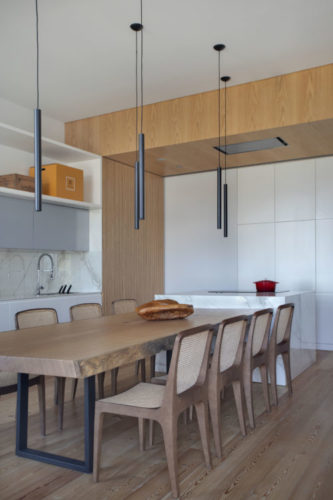 Mesa de jantar em madeira acoplada a ilha do cooktop, na cozinha integrada a sala.