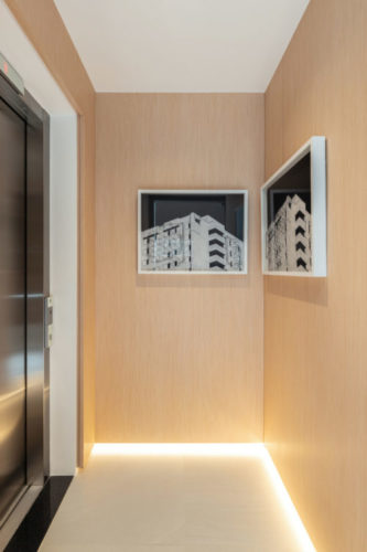 Hall do elevador com a paredes forradas em madeira e uma luz indireta no rodapé