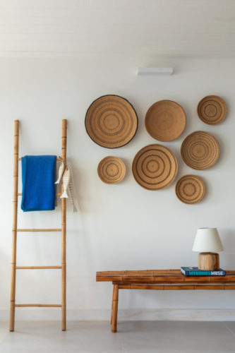 Composição de decoração, banco em madeira com livro, na parede, composição de cestos e ao lado, uma escada em bambu