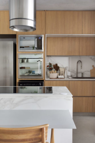 Cozinha aberta para a sala, com armários em madeira clara, torre com eletrodomésticos embutidos na marcenaria 