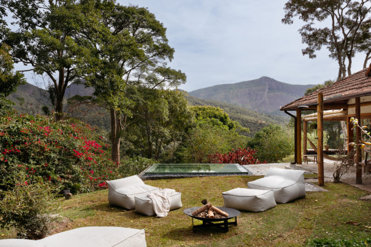 Casa de campo com estética rustica em harmonia com a natureza ao redor. Gramado com piscina e as montanhas ao fundo