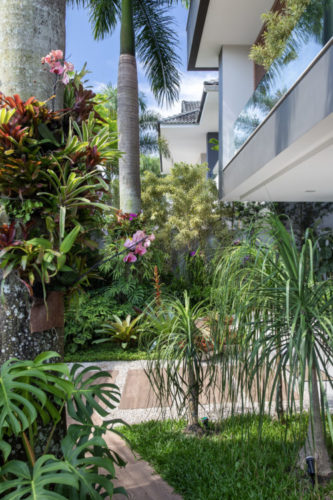 Paisagismo tropical com muitas folhagens, texturas e variedade de vegetação na área externa em uma casa na Barra (RJ)