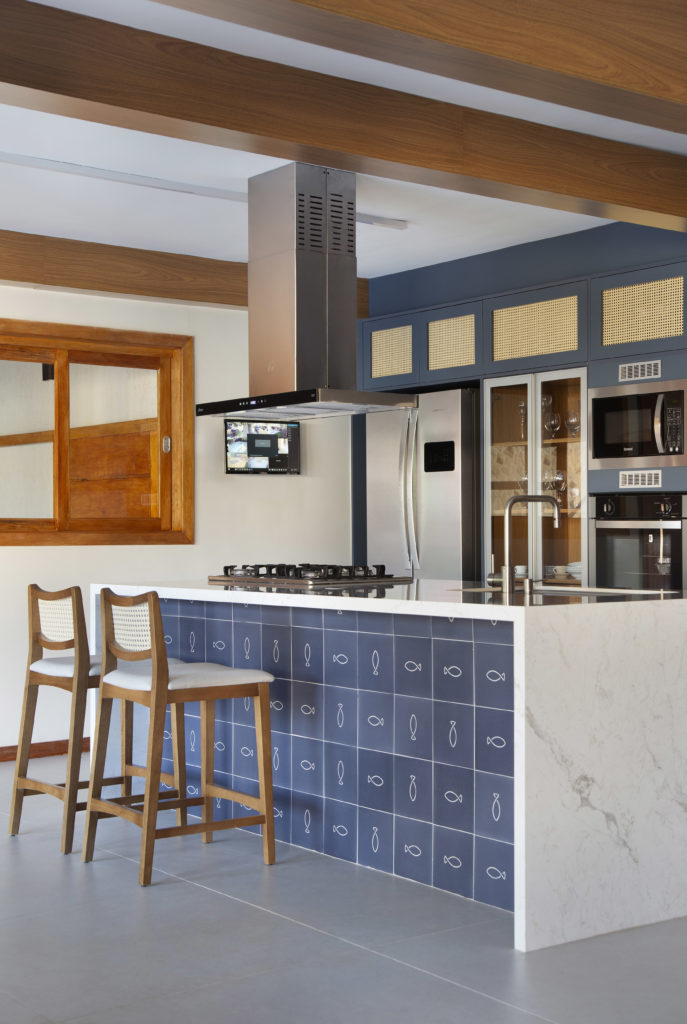 Cozinha da casa, ampla, iluminada e integrada. Uma ilha bancada, com revestimento frontasl em azulejos azuis com desenhos de peixe.