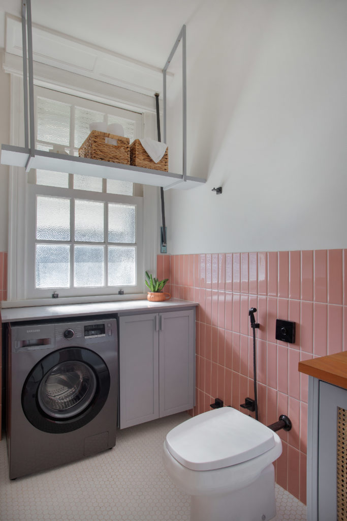 Banheiro com espçao para a máquina de lavar roupas. Nos revestimentos; meia parede com azulejo retangular na cor rosa e piso orignal da época da construção, anos 1940, pastilhas bramcas sextavadas