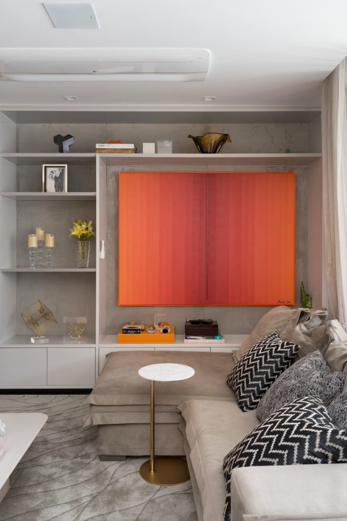 Por dentro do apartamento de uma arquiteta: confira detalhes do projeto de reforma de Ana Rozenblit, que criou uma residência elegante e criativa que mescla o clássico com o moderno. Uma pintura, predominentemente na cor laranja, na estante