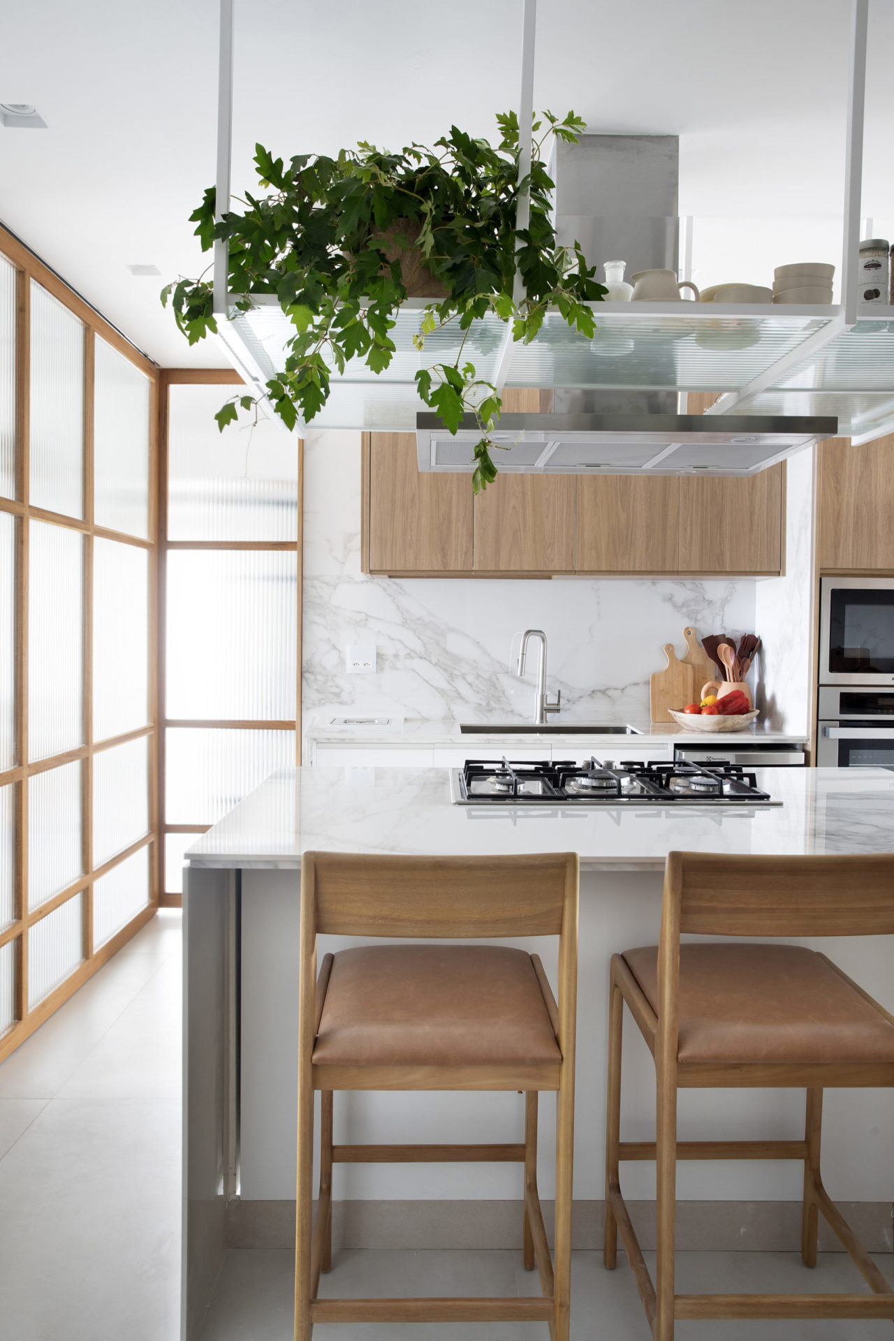 Cozinha claa, com revestimento inspirado no mármore, e portas de correr, que quando abertas, integram os ambientes